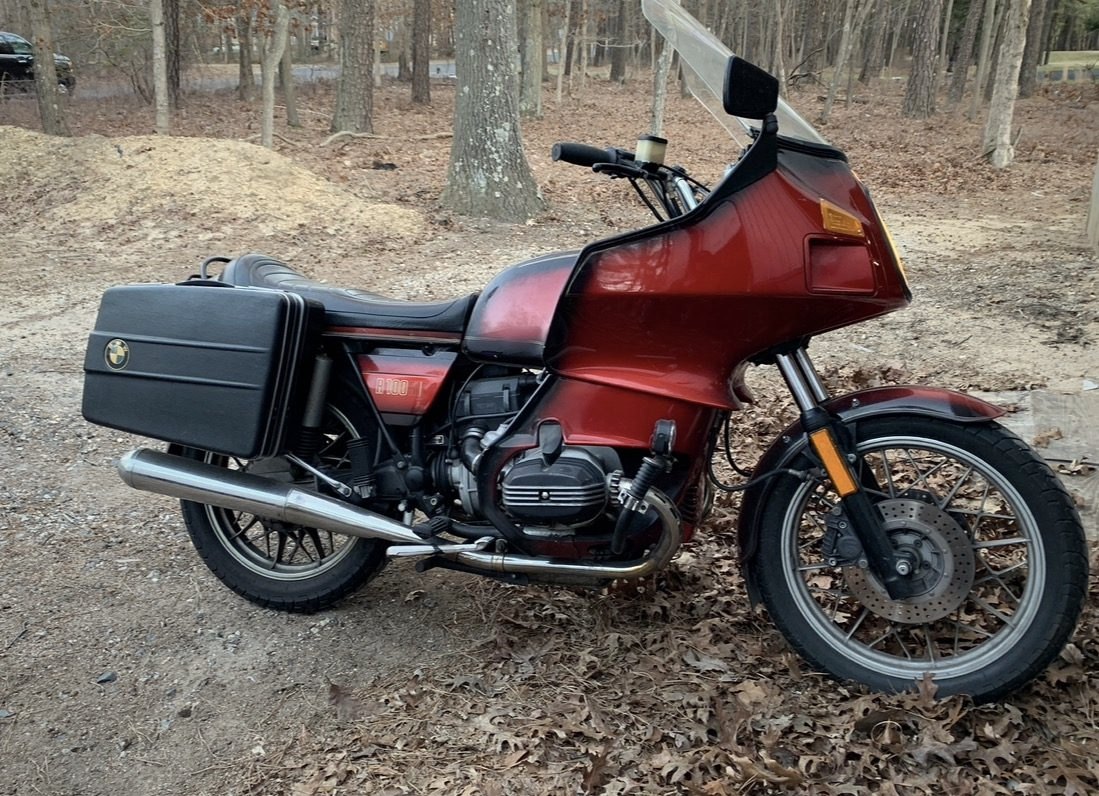 A red 1981 BMW R100RT with full fairing and panniers, parked on leaves