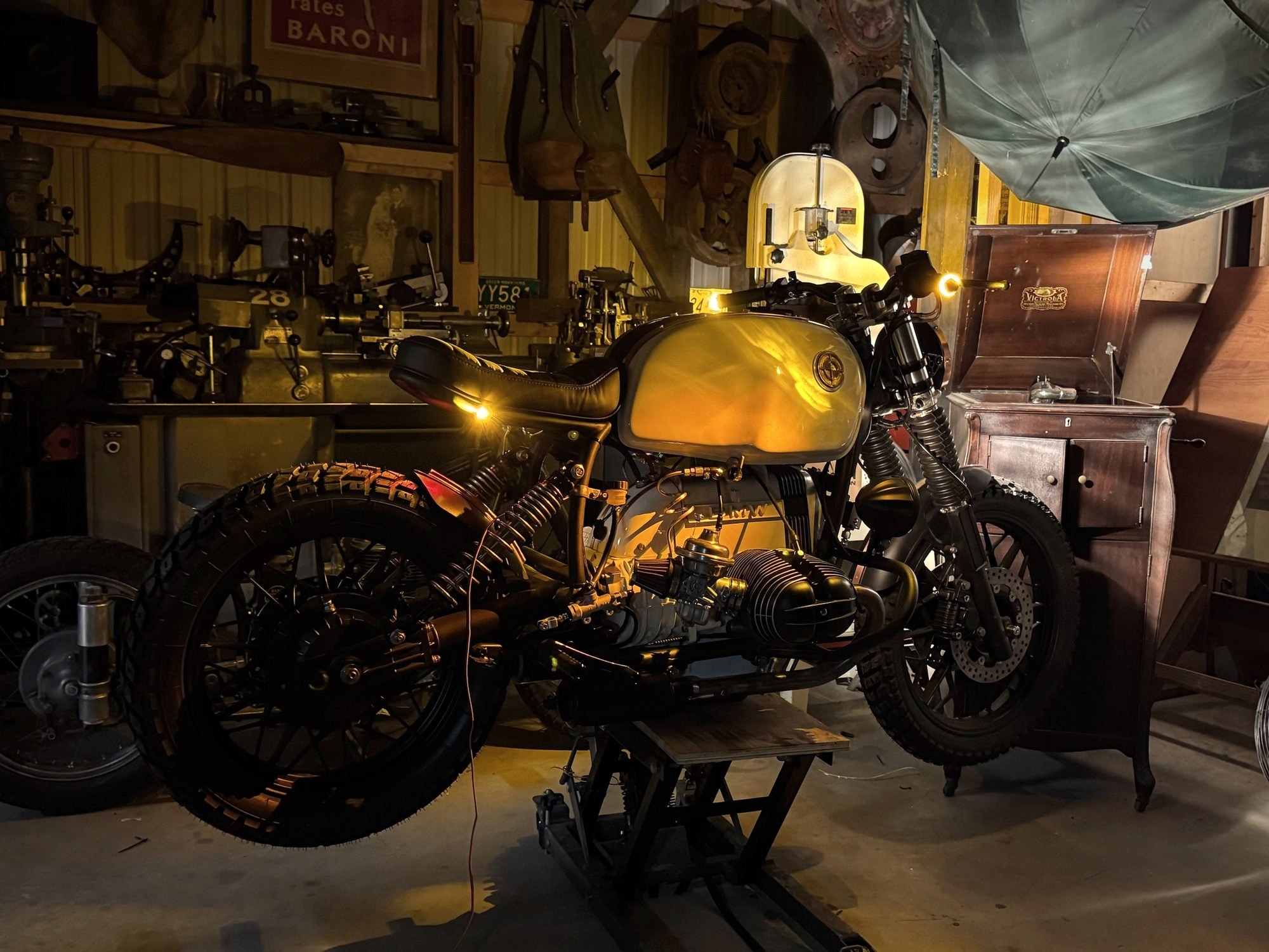 A BMW R100 café racer in a dark workshop, one lamp on the tank