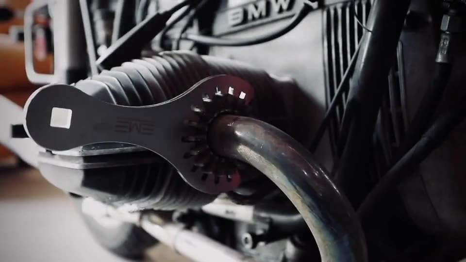 A hand on the exhaust header nut of a BMW airhead, the rear wheel and final drive behind
