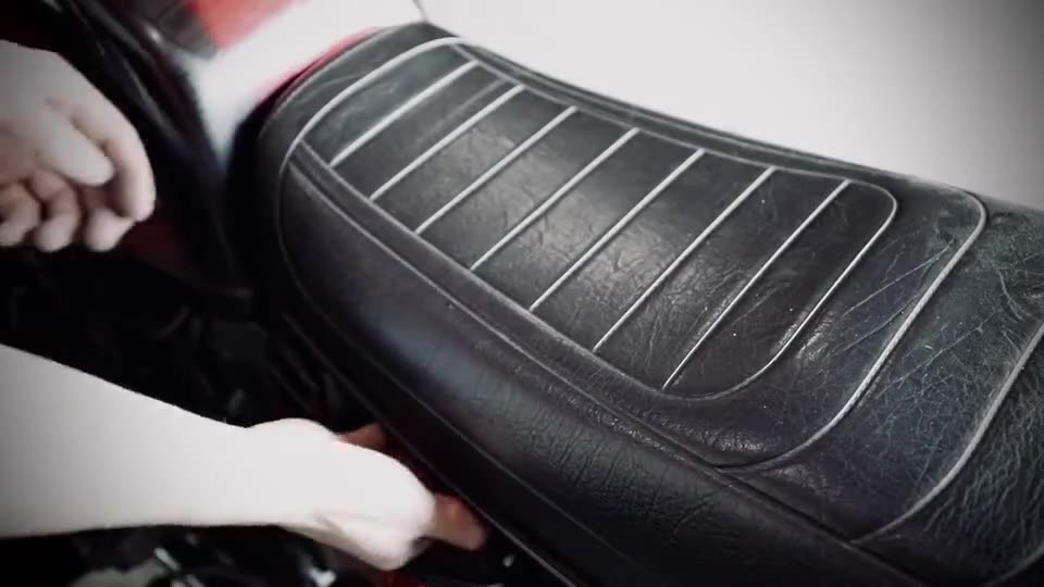 Hands lifting the seat off a red 1981 BMW R100RT in a workshop