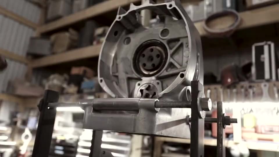 The back of a BMW airhead crankcase on an engine stand, a flywheel being lifted onto the crank flange
